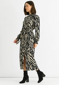 Black and beige zebra-patterned dress with a high neck, long sleeves, and a front slit, paired with black ankle boots.