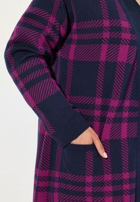 Marinblå cardigan med rosa rutmönster, långa ärmar och sidofickor. Tillverkad av ett mjukt stickat material. Framträdande diagonala ränder.