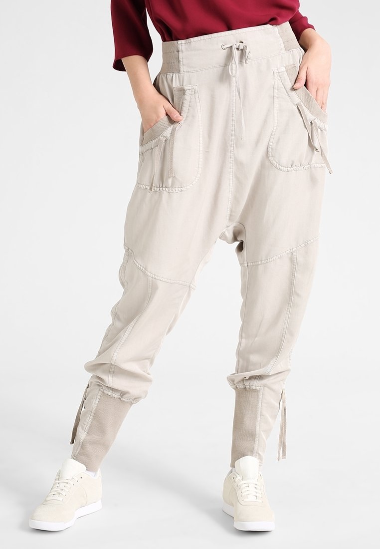 Personne portant un pantalon beige ample avec de grandes poches avant et une taille à cordon, associé à des baskets blanches et un haut rouge.