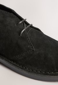 Gros plan d'une chaussure noire en daim à lacets avec des coutures détaillées et une semelle en caoutchouc lisse.