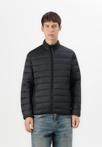 Black puffer jacket with horizontal quilted pattern, high collar, full zip closure, and side pockets, worn over blue denim jeans.
