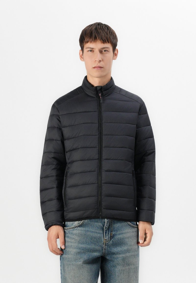 Black puffer jacket with horizontal quilted pattern, high collar, full zip closure, and side pockets, worn over blue denim jeans.