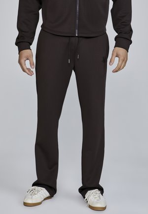 Brown athletic pants made of smooth fabric, featuring a drawstring waist and side pockets. Paired with white sneakers.
