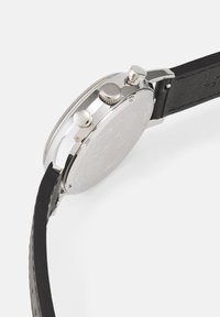 Silver stainless steel watch with a round case, black leather strap, two push buttons, and textured back case.