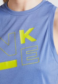 Jasnoniebieska bezrękawnik sportowy z jasnYellowym napisem "NIKE". Materiał wydaje się gładki z subtelnym połyskiem i okrągłym dekoltem.