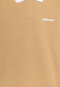 Barna pólóing fehér gallérral, gombos nyakrésszel és egy kis "ellesse" logóval, fehér és piros színben. Sima szövet textúra.