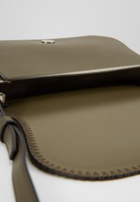 Interno della borsa a tracolla verde oliva in pelle con una texture liscia, caratterizzata da una chiusura a scatto e cuciture a contrasto lungo i bordi.
