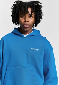 Blue hoodie made of soft fabric with a front pocket. Features a drawstring hood and white "RETERNITY CREATIVE DEPARTMENT" text on the chest.