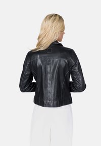 Černá kožená bunda s krátkým střihem, zdobená bílým švem, minimálním kovovým hardwaru a čtvercovou nášivkou na zadní části.