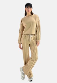 Completo beige composto da una felpa cropped con spalle ribassate e pantaloni a righe con cintura elastica e cordoncino.