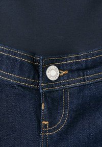 Prim-plan al taliei unei perechi de blugi din denim bleumarin închis, cu nasture argintiu vizibil și cusături contrastante portocalii.