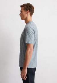 Grijze T-shirt met korte mouwen en een subtiele heather-textuur, ronde halslijn en contrasterende schouderaccenten, weergegeven op een model van opzij.