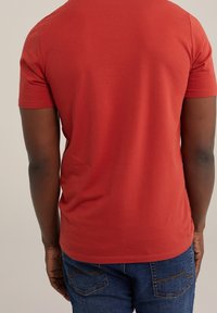 Röd t-shirt med kort ärm, slät textur, figurnära design och rund halsringning, tillsammans med blå denimjeans med bakfickor.