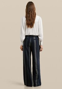 Pantalons larges bleu marine avec des rayures verticales vertes et blanches, fabriqués dans un tissu texturé, assortis à une chemise blanche à manches longues.