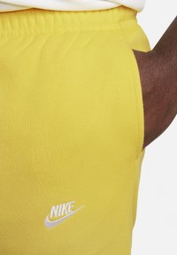 Pantalones de chándal de algodón amarillos con cintura elástica, que presentan un logo de Nike bordado en blanco en el lado izquierdo y una textura suave.