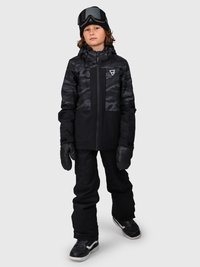 Kind trägt eine schwarze und graue Camouflage-Winterjacke, schwarze Schneehose, schwarze Handschuhe, eine schwarze Mütze und hat Skibrillen auf dem Kopf, steht mit dem Gesicht nach vorne.