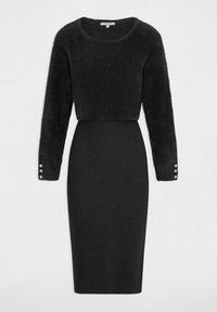 Zwarte jurk met een cropped, fuzzy trui met lange mouwen en een rib gebreide kokerrok. Details met knopen bij de mouwranden.
