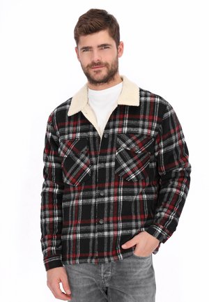 Kurtka w kratę wykonana z flanelowej tkaniny, z czarno-czerwono-szarymi wzorami, kremowym kołnierzem typu sherpa oraz dwoma kieszeniami na piersi z patkami.