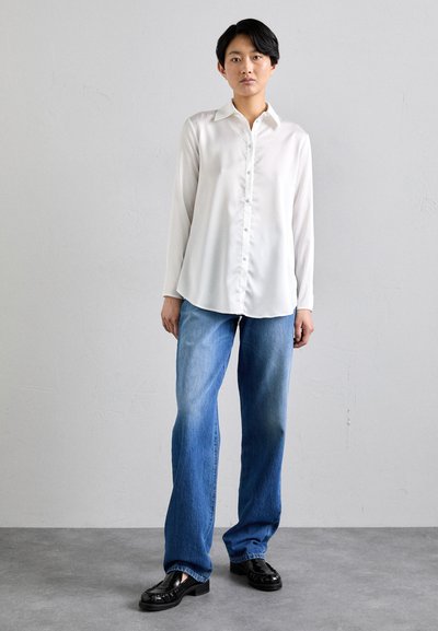 White satin long-sleeve shirt with button closure, paired with light blue denim wide-leg jeans and black glossy loafers on a neutral background.