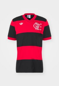 Röd och svart randig fotbollströja med v-ringning, Adidas-logotyp på vänster axel och laglogotyp med stjärnor på bröstet.