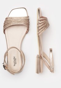 Metallisch goldene flache Sandalen mit geflochtenen Riemen, quadratförmiger Zehenpartie und Knöchelverschluss. Strukturiertes Stoffdetail und eine klobige Zwischensohle.