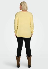 Pull en grosse maille jaune surdimensionné avec poignets et ourlet côtelés, associé à un jean skinny noir et des bottes de cowboy marron. Texture douce, design décontracté.