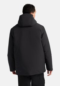 Doudoune noire avec capuche, offrant une texture douce et lisse, des manches longues et des poignets à boutons-pression. Conçue pour l'isolation et la chaleur.