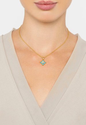 Gold chain necklace featuring a floral pendant with four turquoise stones and gold accents, set against a neutral fabric background.