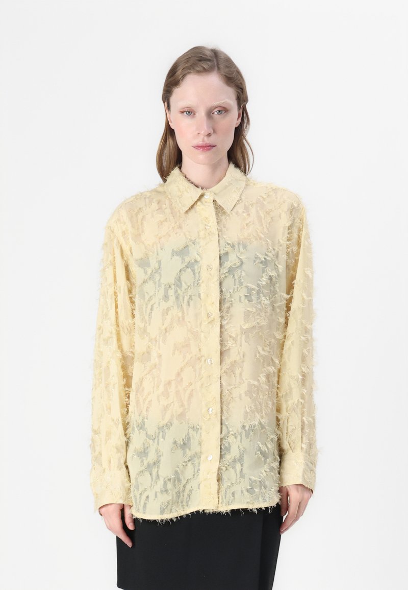 Translucent yellow shirt with textured floral pattern, long sleeves, and button-down front. Worn over a black bottom.