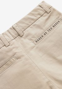 Beige trousers with belt loops and a back pocket featuring a stitched label that reads "BAKER BY TED BAKER."