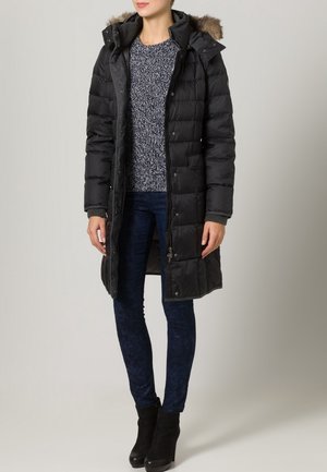 Black puffer coat with a fur-trimmed hood, zip and snap closure, quilted texture, paired with a knit sweater and dark denim jeans.