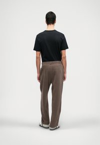 Brūni flīsa sporta bikses ar elastīgu jostasvīru. Apvienotas ar melnu īsām piedurknēm T-kreklu un pelēkiem čību. Skats no aizmugures.