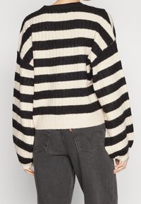 Czarny i kremowy prążkowany sweter w paski z okrągłym dekoltem i bufiastymi rękawami, zestawiony z ciemnoszarymi jeansami z tylnymi kieszeniami.