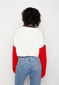Pull court avec des couleurs alternées blanc, rouge et marine. Texture en tricot à torsades sur le blanc, manches rouges lisses et ourlet côtelé.