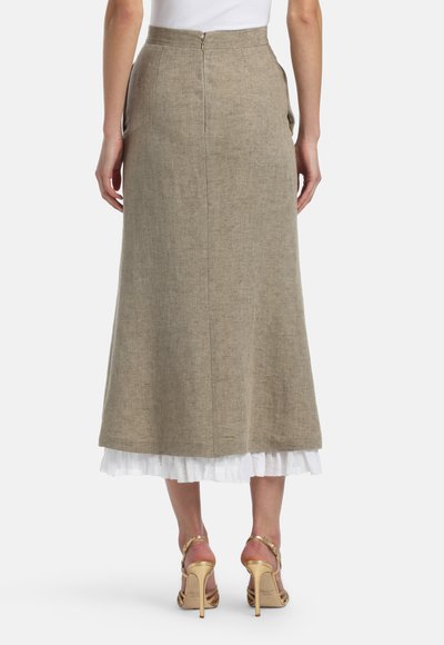 Woman wearing a beige midi skirt with a back zipper over a white layered skirt, paired with gold high-heeled sandals, shown from the back.