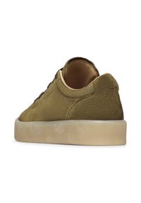 Scarpa da ginnastica in suede verde oliva con suola in gomma traslucida beige spessa, taglio alla caviglia basso e lacci marroni visti da un angolo posteriore.