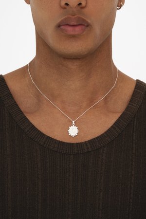 Primo piano di una persona che indossa una collana con pendente a raggiera d'argento e un maglione marrone a coste con scollo a V, mostrando collo e parte superiore del petto.