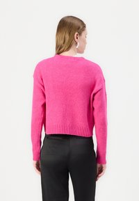 Fluffy, cropped sweateri kirkas vaaleanpunainen, jossa on pyöreä pääntie ja ribatut hihansuut, yhdistetty mustiin muotopaitoihin.