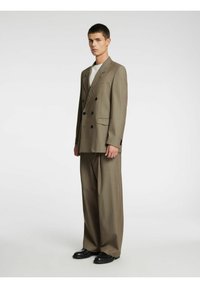 Divrindu uzvalks gaiši brūnā audumā ar platajam biksēm. Aprīkots ar melnām pogām un izgriezuma atloku. Kombinēts ar baltu kreklu.