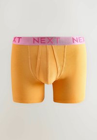 Sárga pamut boxeralsó, rózsaszín rugalmas derékpánttal, amelyen a "NEXT" szó van gravírozva. Jól illeszkedő fazonja van, és varrási részletei vannak.