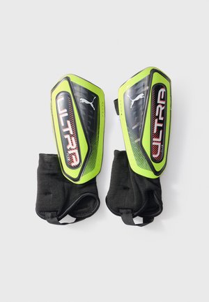 Pair of neon green and black Puma Ultra Flex soccer shin guards with black ankle sleeves on a light background.