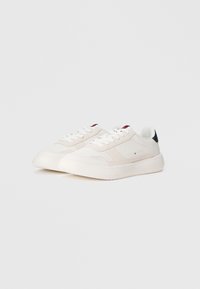 Hvide sneakers med en glat læder- og ruskinds-overdel, der har en struktureret tåhætte og en mørkeblå detalje på hælen. Flade hvide snørebånd.
