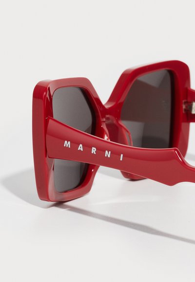 Occhiali da sole oversize rossi con una finitura lucida, dotati di montature spesse, lenti scure e logo "MARNI" in bianco sulla tempia.