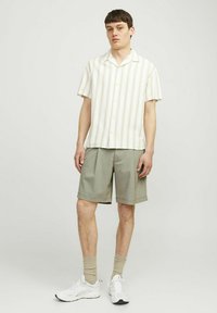 Chemise à manches courtes rayée en crème et vert, associée à un short gris, des baskets blanches et des chaussettes beiges, offrant une coupe décontractée.