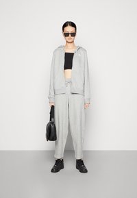 Grå hettegenser og matchende bukser laget av mykt materiale, svart crop top, svarte solbriller, og en svart crossbody veske.