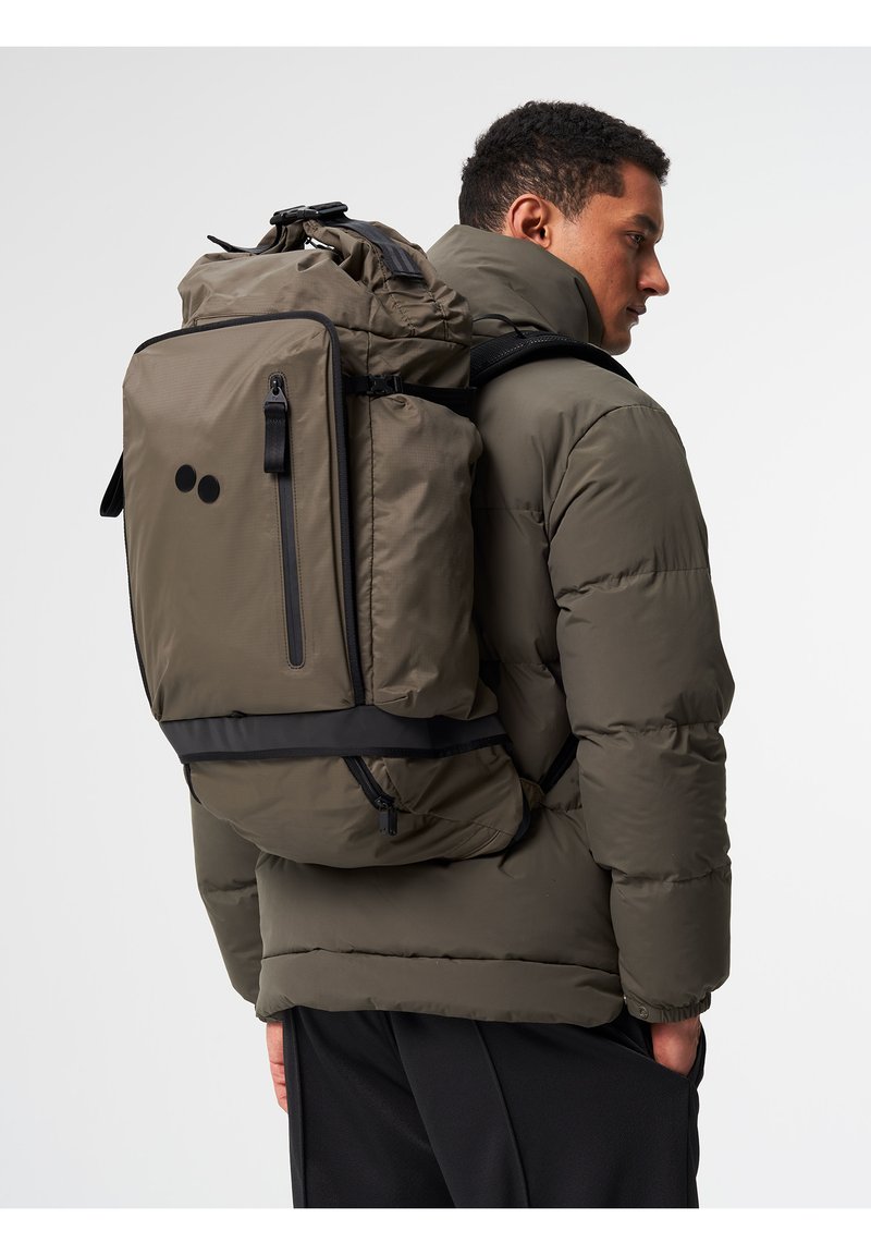 Olivgrüner Rucksack mit strukturiertem Design, zwei schwarzen Punkten, verstellbaren Trägern und mehreren mit Reißverschluss versehenen Fächern.