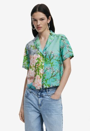 Kurzärmliges, button-up Hemd mit grünen, rosa und blauen Blumenmustern, versehen mit einem Kragen und einem lässigen Schnitt, getragen zu hellblauen Jeans.