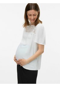 Graviditetsblus i vitt med texturerat tyg, med en spetsdesign vid halsringningen och korta, vida ärmar. Matchad med en svart kjol.