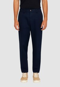 Pantaloni blu navy dal taglio dritto, realizzati in tessuto liscio, con chiusura frontale con bottoni e tasche laterali, indossati con sneaker beige.