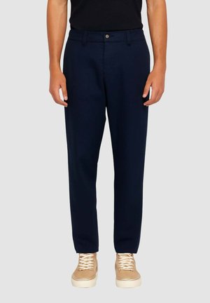 Pantaloni blu navy dal taglio dritto, realizzati in tessuto liscio, con chiusura frontale con bottoni e tasche laterali, indossati con sneaker beige.